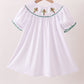 White dress with green trim and red embroidery on a hanger against a beige background